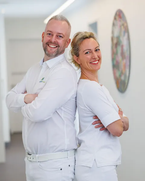 Dr. Daniel Dietrich und Dr. Ivonne Seiling-Dietrich stehen Rücken an Rücken im Praxisflur und lachen